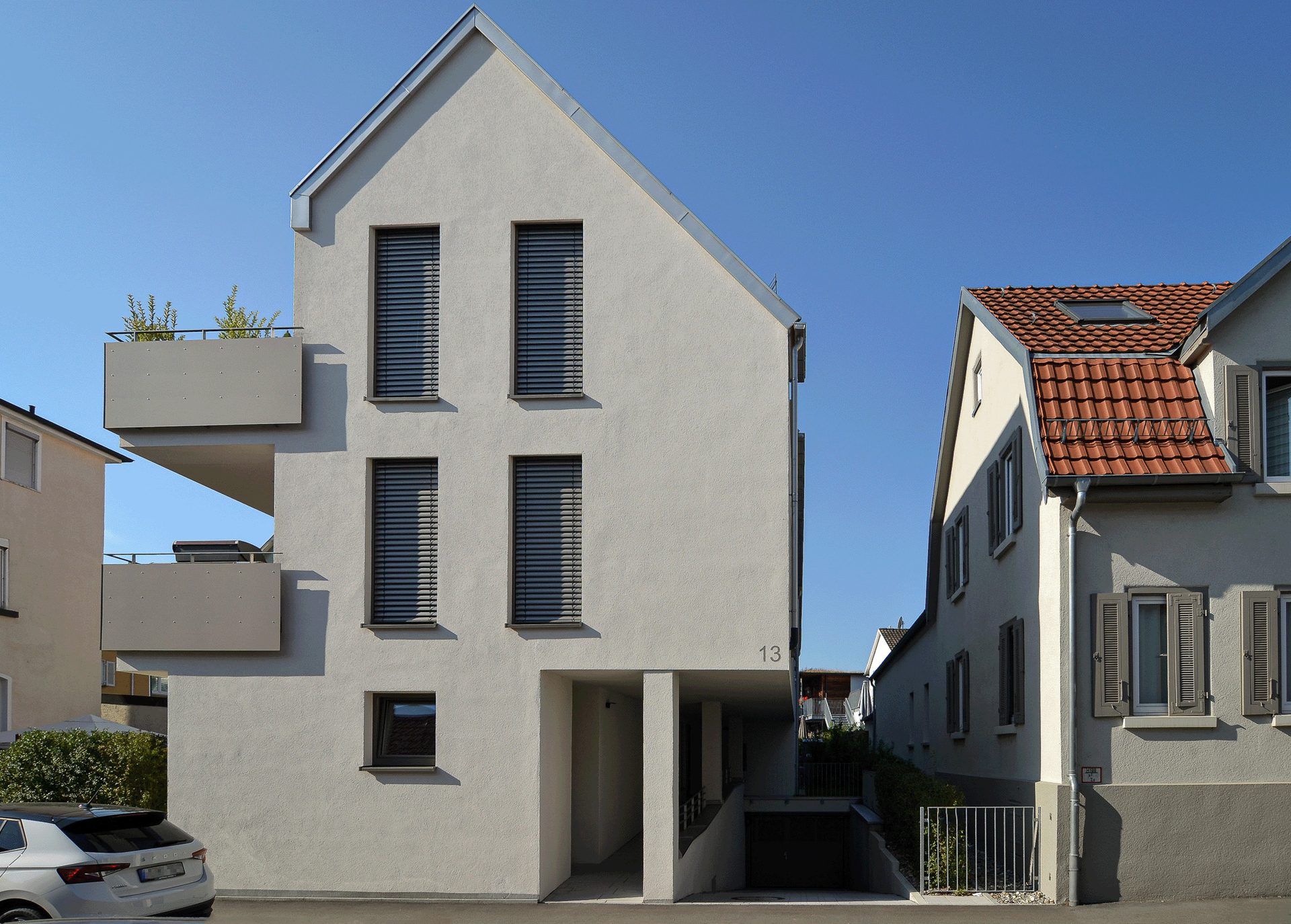 Weiss verputzte Fassade eines Neubaus von Kraft Consulting mit dunklen Raffstoren